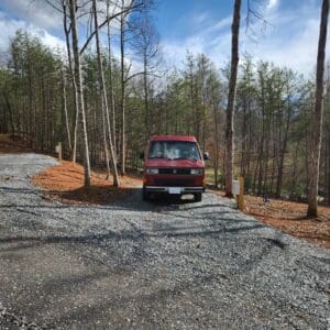 A van parked on the side of a road in the woods.