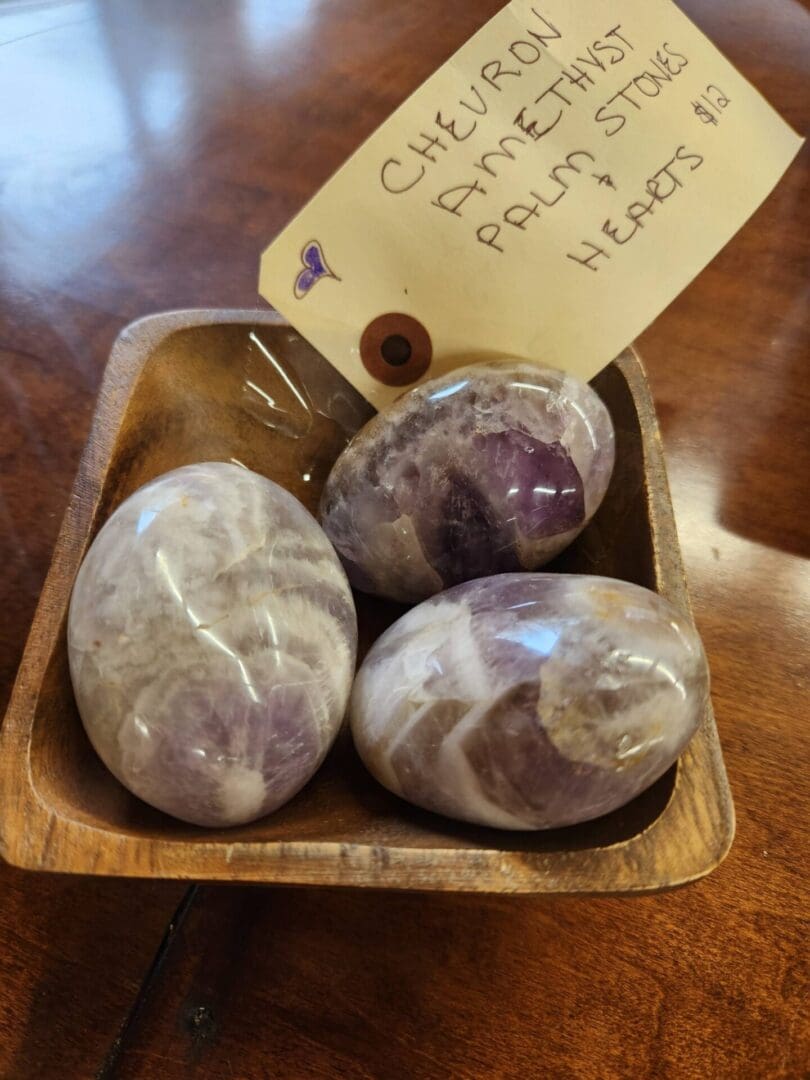 A wooden bowl with three purple and white stones.