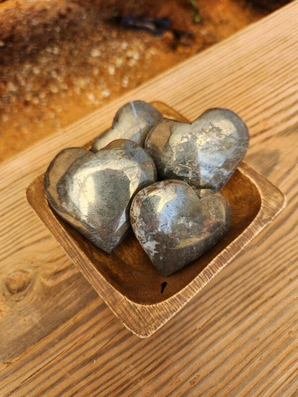 A wooden bowl with four metal hearts in it.